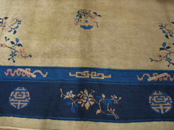 Beige rug with dark blue borders featuring peach floral designs, light blue accents, and key pattern elements.