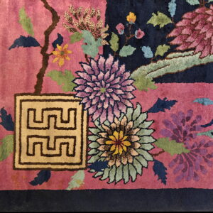 Close-up of a high-pile rug with a rose field, navy contrast, colorful flowers, and a beige geometric symbol.