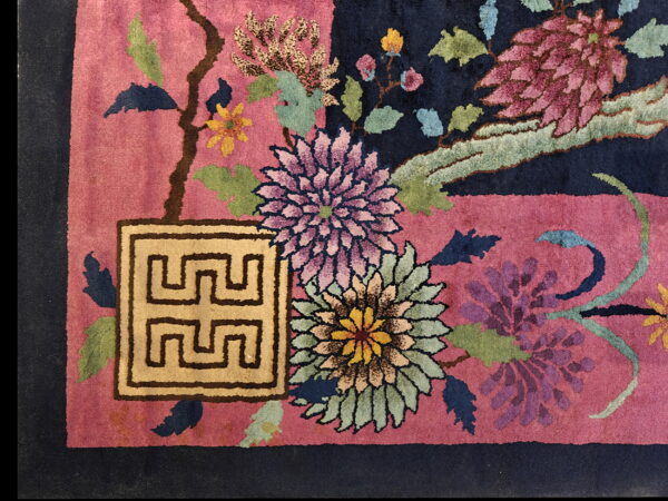 Close-up of a high-pile rug with a rose field, navy contrast, colorful flowers, and a beige geometric symbol.