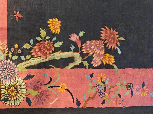 Plush rug detail showing stylized multicolored floral motifs on a dark field and wide dusty rose border.