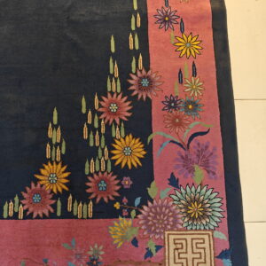 Navy blue rug corner with a thick rose border features multicolored floral designs and a beige square geometric motif.