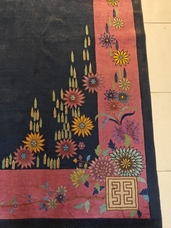 Navy blue rug corner with a thick rose border features multicolored floral designs and a beige square geometric motif.