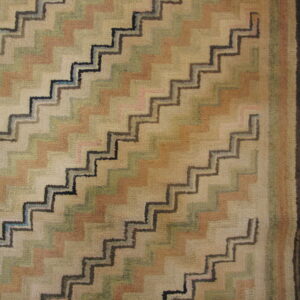 Muted zigzag pattern rug in beige, sage, and tan with dark outlines, next to natural wood plank flooring.