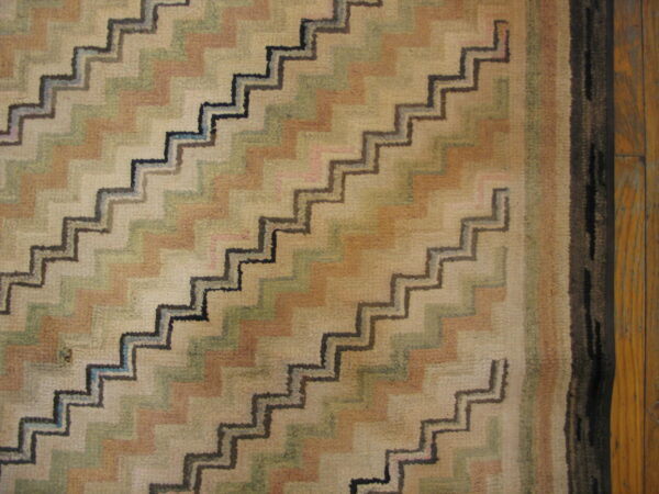 Muted zigzag pattern rug in beige, sage, and tan with dark outlines, next to natural wood plank flooring.