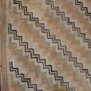 A textured, colorful rug featuring large diagonal stepped zig-zags rests on wood plank flooring.