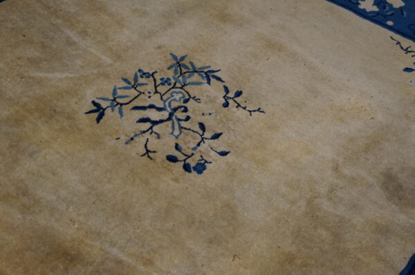 Close detail of a soft beige rug with an intricate two-tone blue floral branch design.