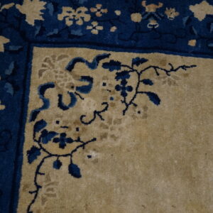 High-pile rug corner in tan and navy blue with detailed vine and floral border motifs.