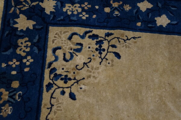 High-pile rug corner in tan and navy blue with detailed vine and floral border motifs.