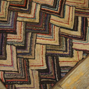 Multicolored textured rug with a dark zigzag pattern on a light background, resting on worn wood planks.