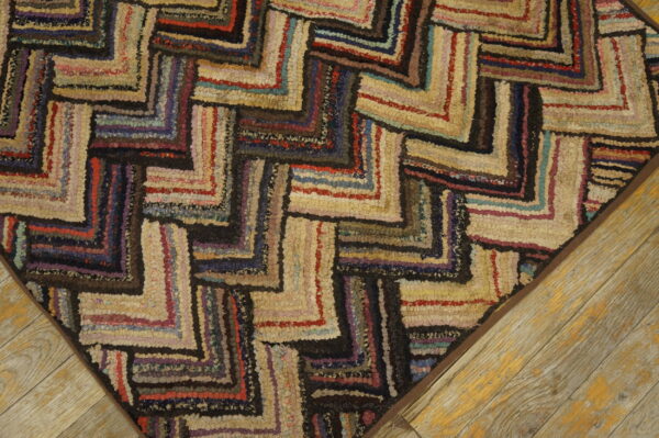 Multicolored textured rug with a dark zigzag pattern on a light background, resting on worn wood planks.