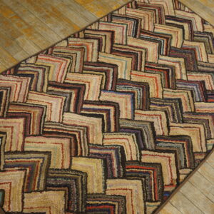 Textured multicolored rug with an interlocking log cabin pattern rests on weathered wood planks.