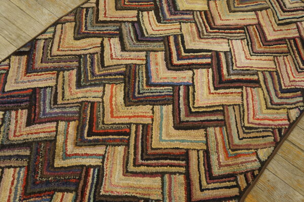 A deeply textured, multi-colored hooked rug with a zigzag geometric pattern sits on wood planks.