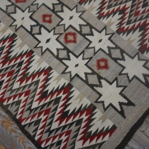 Cream, gray, and red geometric rug with zigzag patterns and stars resting on distressed wood planks.