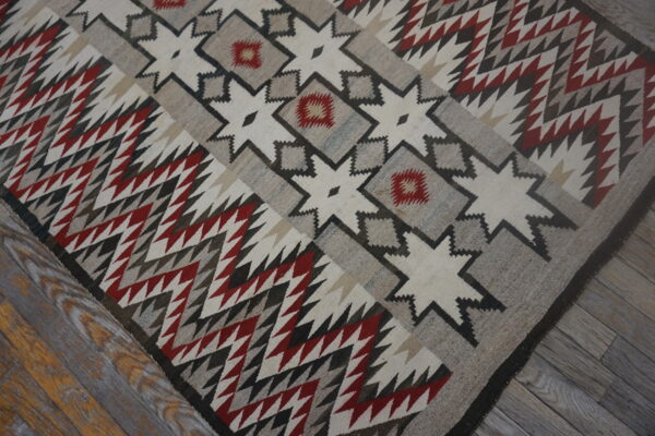 Cream, gray, and red geometric rug with zigzag patterns and stars resting on distressed wood planks.
