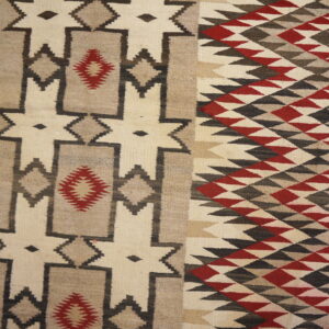 Flatweave rug displaying cream, brown, charcoal, and red geometric diamonds and stepped designs near wood planks.