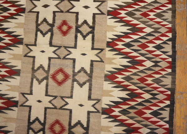 Flatweave rug displaying cream, brown, charcoal, and red geometric diamonds and stepped designs near wood planks.