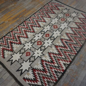Flatweave rug featuring central geometric stars and zigzag borders in red, gray, cream, and black on wood plank flooring.