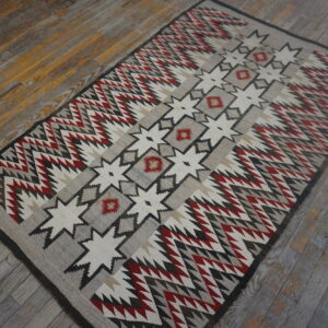 Geometric rug in gray, red, and white tones featuring a central star design on aged wood floors.