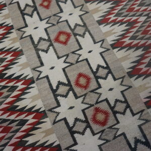 Flatwoven geometric rug in red, black, gray, and cream resting on wood flooring.