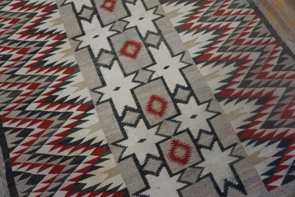 Flatwoven geometric rug in red, black, gray, and cream resting on wood flooring.