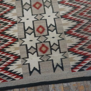 Flat woven rug with red, black, gray, and cream geometric designs sits on worn wood flooring.