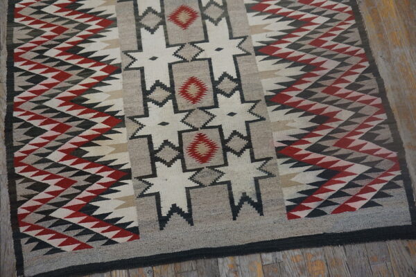 Flat woven rug with red, black, gray, and cream geometric designs sits on worn wood flooring.