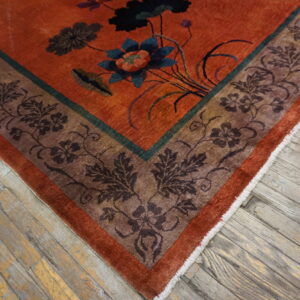 Rust orange rug with deep green and brown floral patterns rests on aged wooden floorboards.