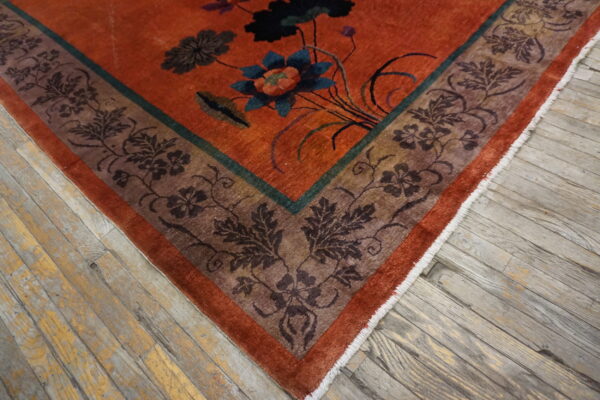 Rust orange rug with deep green and brown floral patterns rests on aged wooden floorboards.