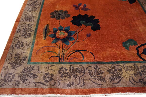 Close-up of a rust-colored rug featuring stylized blue and black floral motifs and a detailed taupe and brown border.