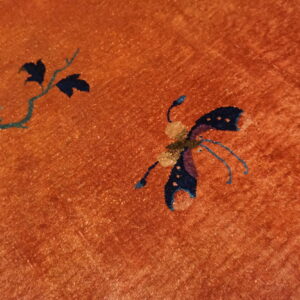 Detailed view of an orange rug with blue butterfly and green vine motifs.