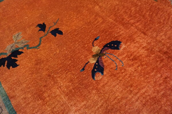 Detailed view of an orange rug with blue butterfly and green vine motifs.