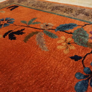 Vibrant orange rug detail showing multi-colored floral vines and a decorative brown and teal border.