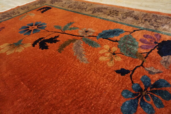 Vibrant orange rug detail showing multi-colored floral vines and a decorative brown and teal border.