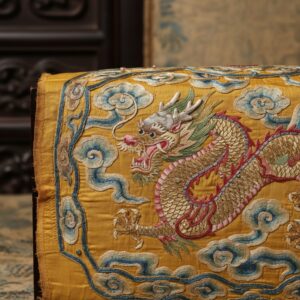 Close-up of intricate gold thread embroidery depicting a dragon amidst blue and white clouds on yellow silk – by rugs on net