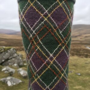 Close-up of a knitted textile featuring a green, purple, and orange argyle diamond pattern against a blurred moorland background – by rugs on net