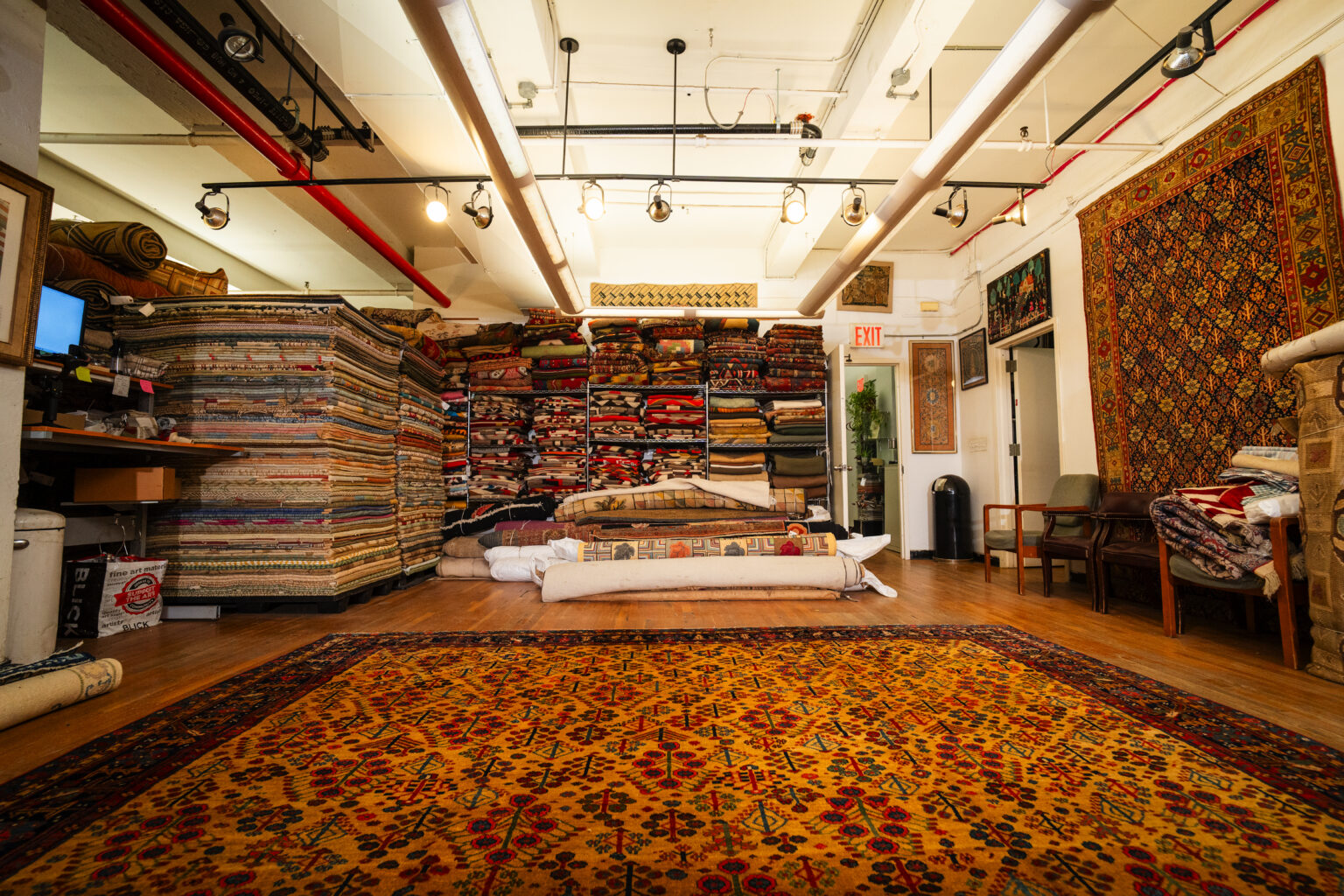 The rugs on net showroom on east 31st street: stacked antique rugs and a room-size persian carpet on the floor