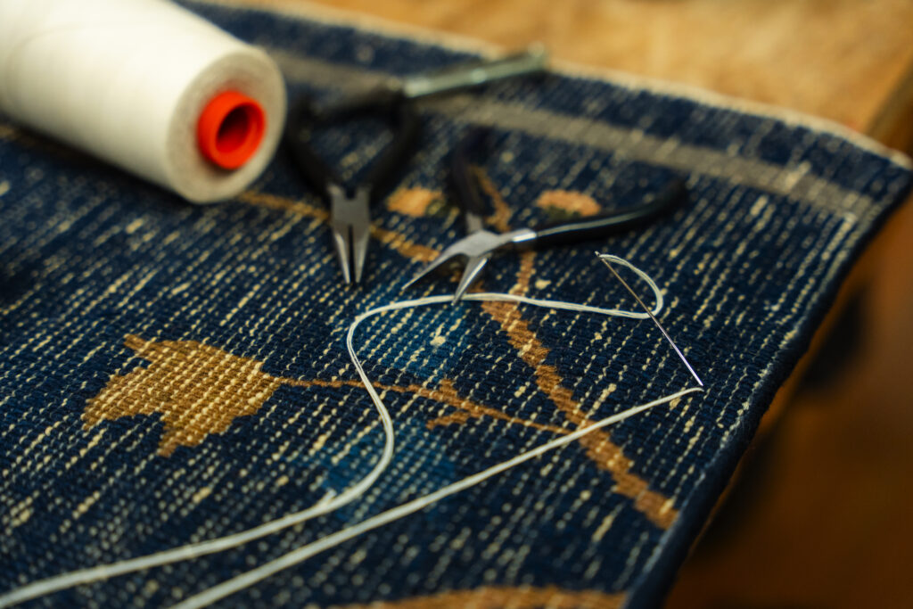 Expert rug repair and restoration services 3 Tools and thread laying on a blue handmade rug showing natural abrash