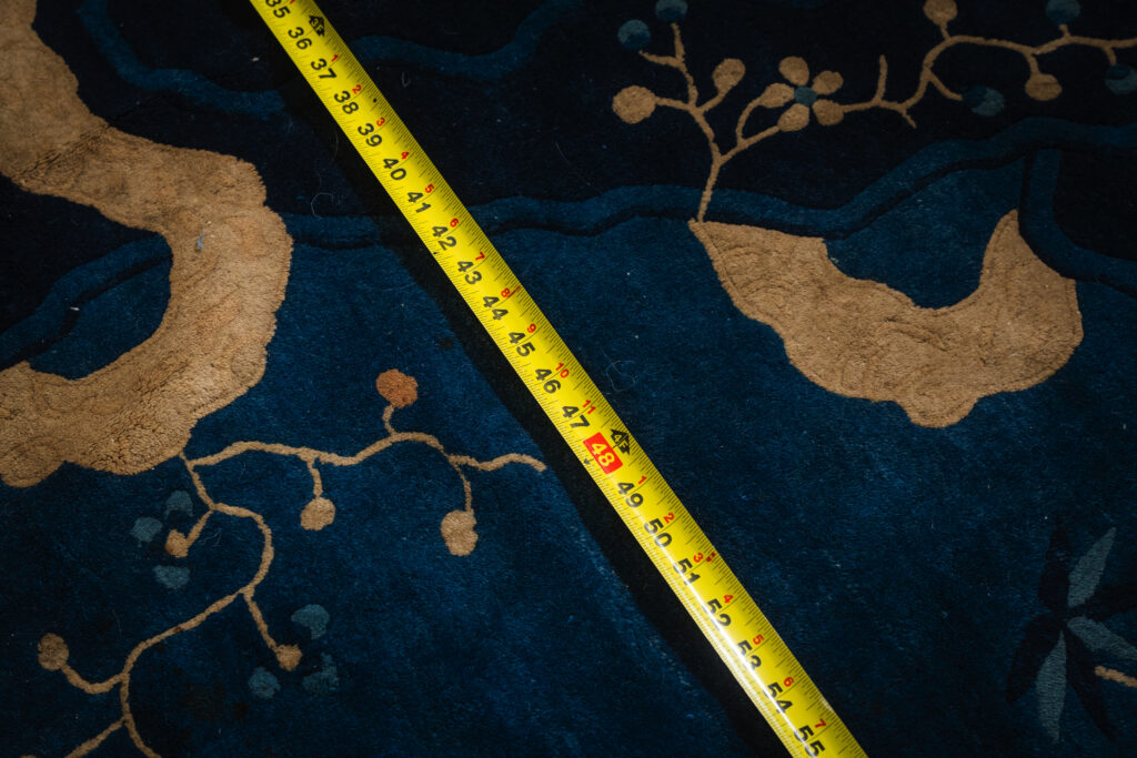 Measuring the width of a blue handmade rug with a tape measure