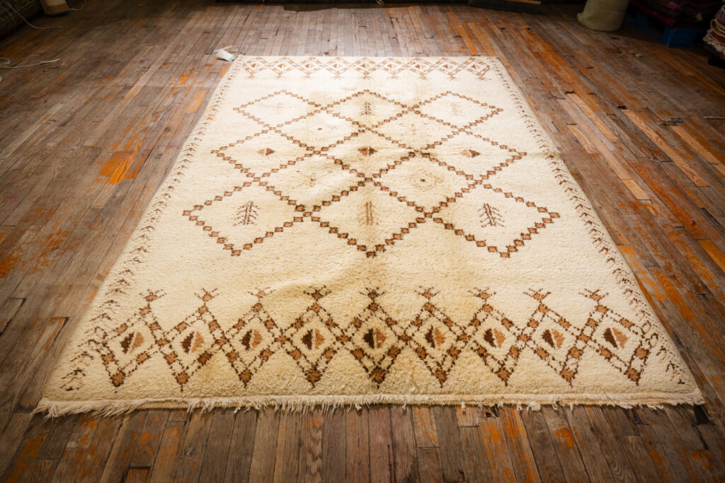 ivory Moroccan-style vintage rug with brown geometric pattern laid on wooden floor