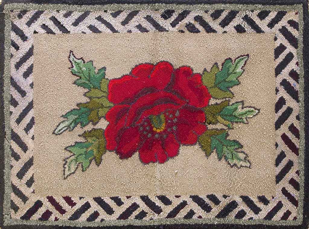 A rectangular, antique hooked rug featuring a large, vibrant red rose with green leaves centered on an ivory field, surrounded by a geometric lattice border, by rugs on net.