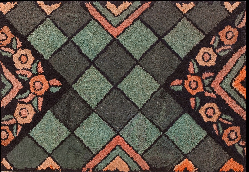 Close-up of an antique hooked rug featuring a central diamond lattice pattern in dark gray and teal, accented by salmon-pink stylized floral motifs along the border area by rugs on net.