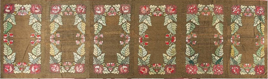 A long, horizontal antique hooked rug with a brown background featuring repeating rectangular borders made of large pink and red roses and green leaves by rugs on net.