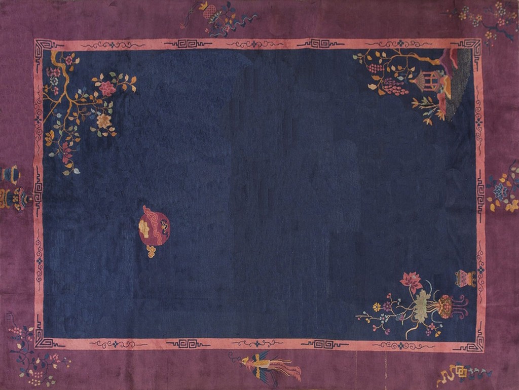 An antique room-size rug with a deep navy blue center field surrounded by a fuschia border and salmon-colored inner framing. The rug features scattered, stylized floral and lantern motifs in pastel colors, characteristic of art deco oriental design by rugs on net.