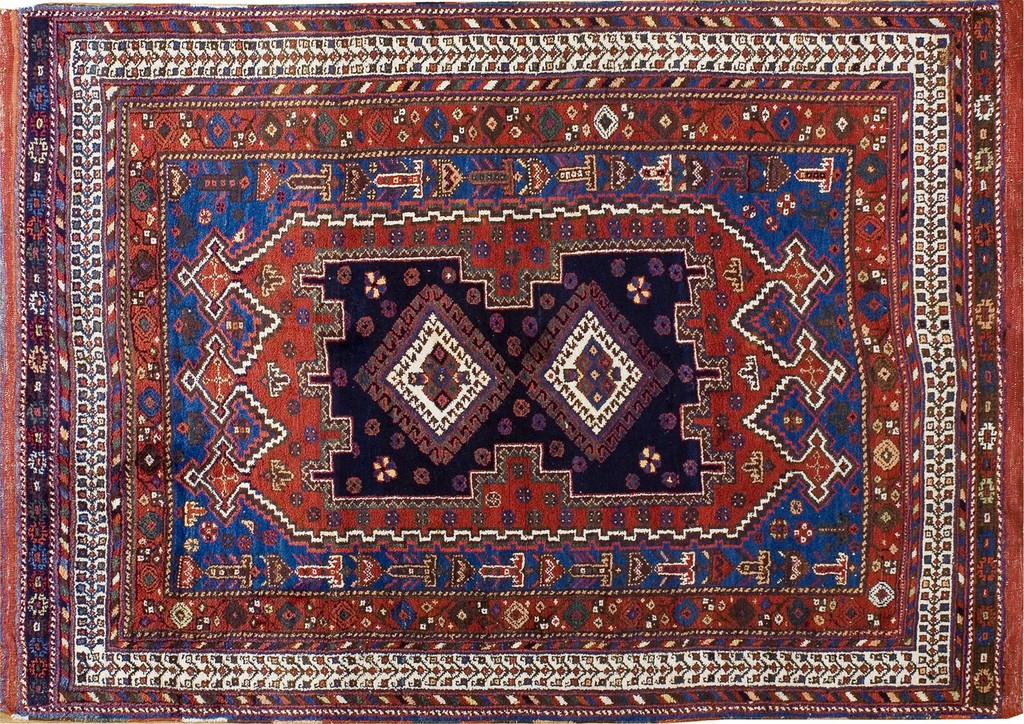 A rectangular, hand-knotted wool rug from the 1930s featuring bold geometric medallions in deep navy blue and rich terracotta red, framed by complex decorative borders by rugs on net.