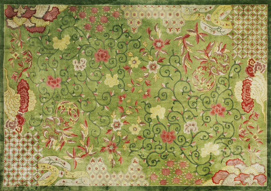 A rectangular antique chinese art deco rug featuring a lush green field densely covered in dark vine scrolls and scattered pink, yellow, and cream flowers, with geometric pattern accents in the corners and borders, by rugs on net.