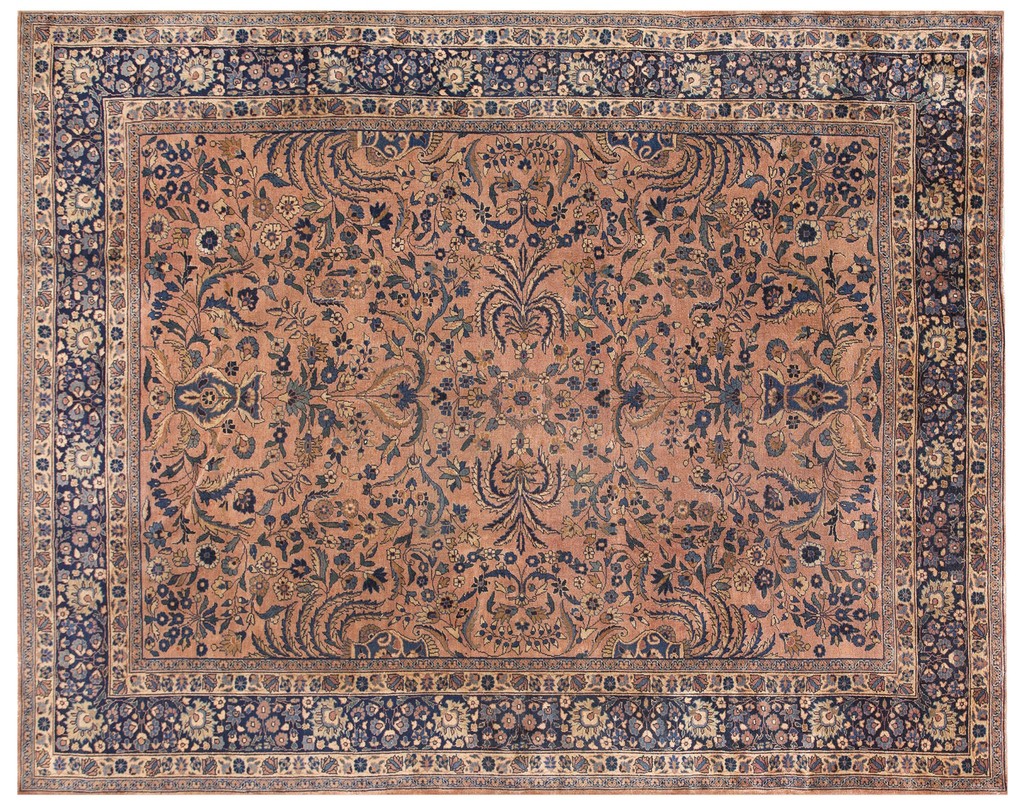 An overhead view of an antique persian mashad room-size rug featuring a complex all-over floral pattern in navy blue on a dusty coral field, surrounded by a thick navy blue border by rugs on net.