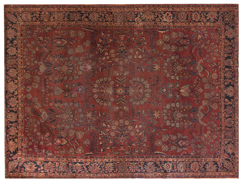 An overhead view of a large antique persian sarouk rug featuring a deep coral red field with all-over muted floral patterns in blues and golds, framed by a dark navy border by rugs on net.