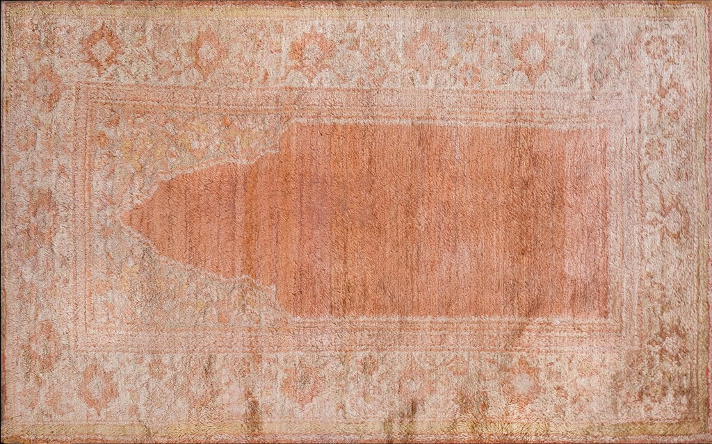 An antique oushak prayer rug featuring a large central field in faded salmon-pink with an ornate, subtly patterned border in muted ivory and rose tones by rugs on net.