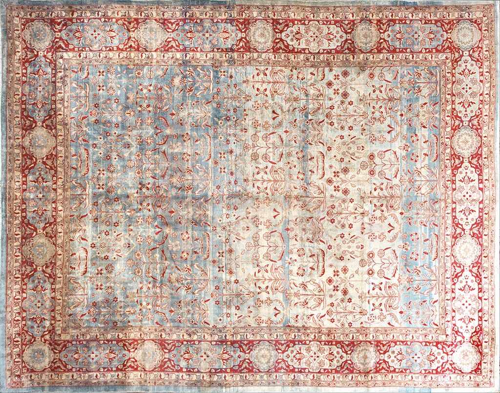Overhead view of a large, rectangular antique lahore indian knotted shah abbas design rug featuring a faded light blue and cream field with red floral patterns, surrounded by a wide, intricate red and cream border. By rugs on net