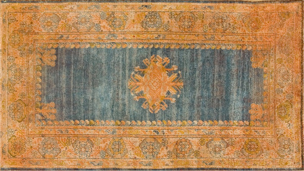 An antique oushak runner rug featuring a deep, striated blue center field with a large orange medallion, framed by a wide, warm orange and gold floral border by rugs on net.